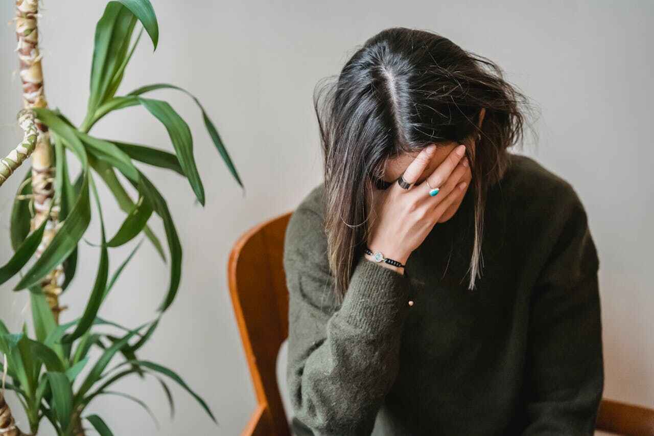 Pregnant woman sitting on a couch with her hand on her forehead, experiencing stress during the first trimester.