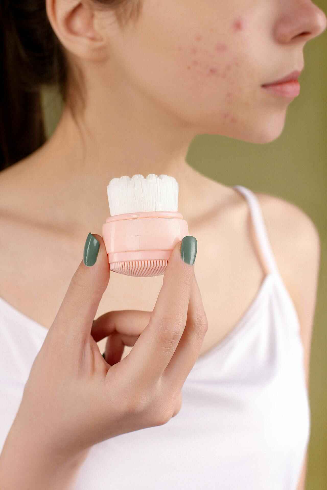 A woman applying a soothing face mask, part of a winter skincare routine for acne-prone skin.