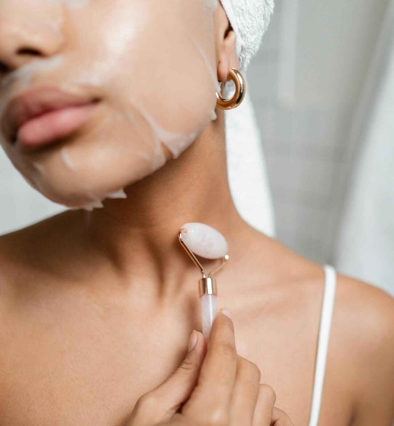 A woman with a towel on her head massaging her face while wearing a hydrating face mask.