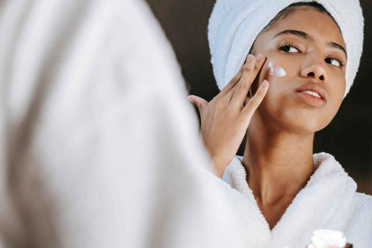 A woman with a towel on her head applying moisturizer as part of her winter skincare routine.